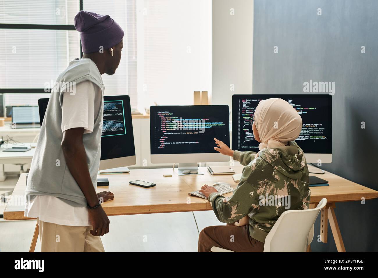 Young confident Muslim woman in hijab making presentation of decoded data on computer screen to African American male colleague Stock Photo