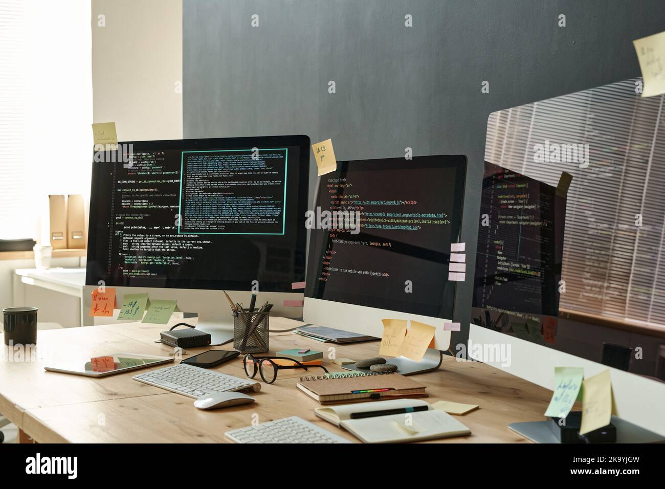 Group of monitors with coded data and sticky notepapers on screens standing on wooden table in office of modern IT engineers Stock Photo