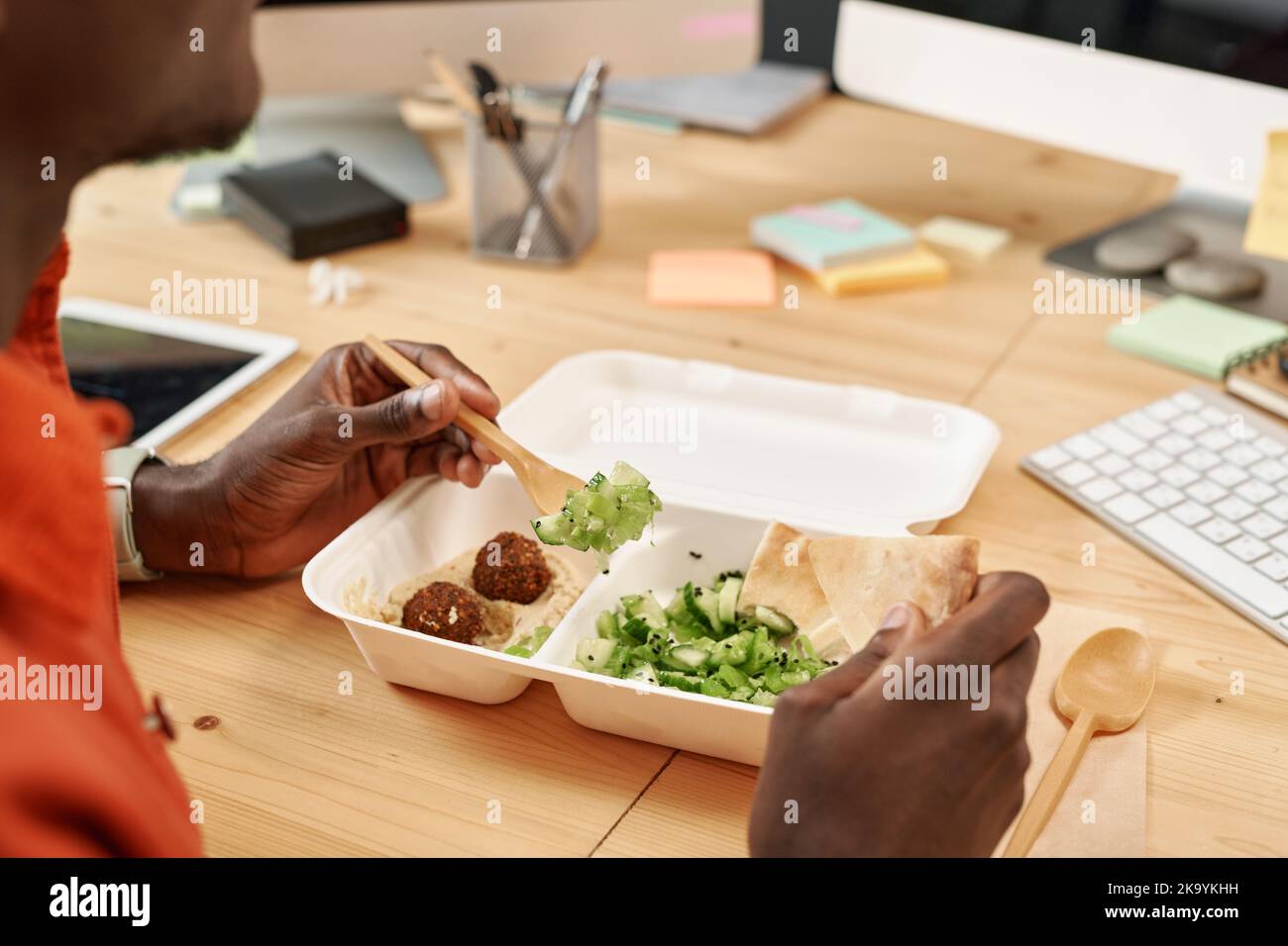 Close-up of eco package with vegetarian food and hands of hungry young African American office worker having lunch by workplace Stock Photo