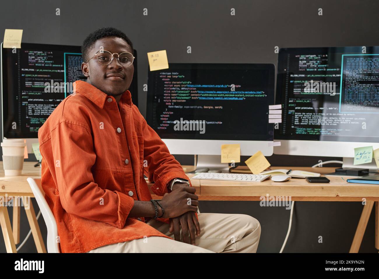 Young IT support manager looking at camera while sitting by workplace in front of computer monitors with decoded data on screens Stock Photo