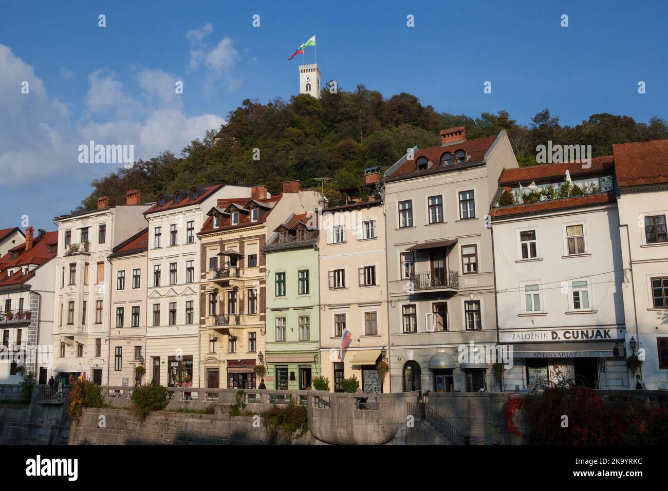 Houses and shop fronts beside the Ljubljana River with Ljubljana Castle in the background, Slovenia Stock Photo