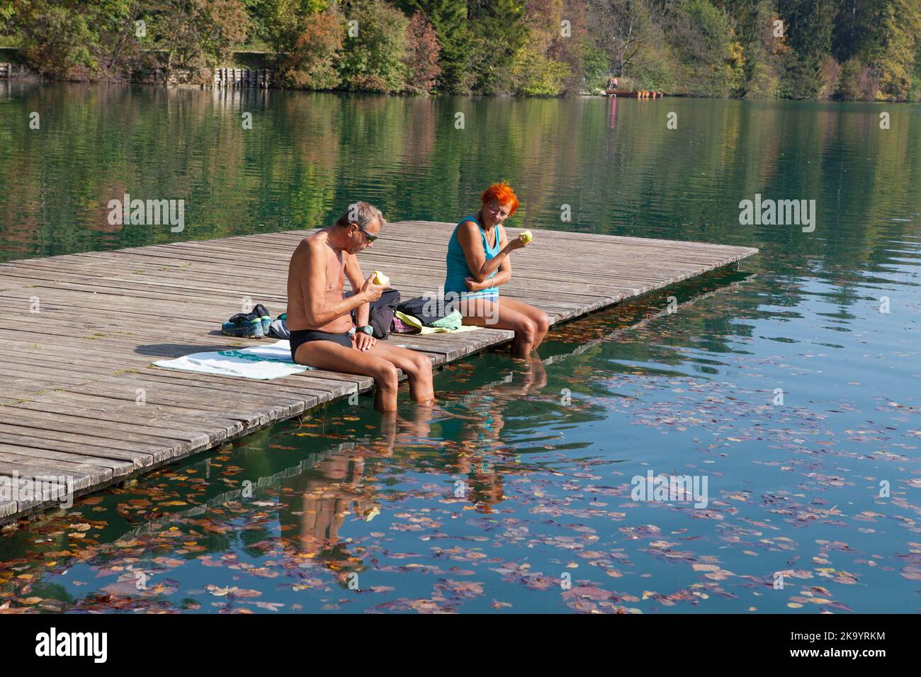 An elderly couple sunbathe & picnic at Lake Bled, Slovenia Stock Photo