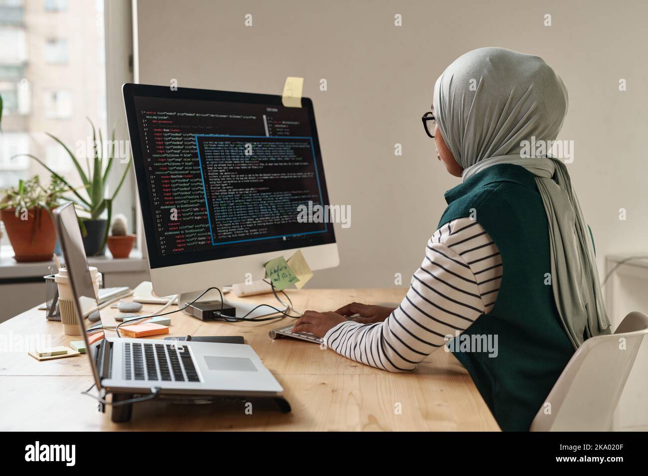 Young Muslim businesswoman or intern looking at computer screen while typing and decoding data or developing software by workplace Stock Photo
