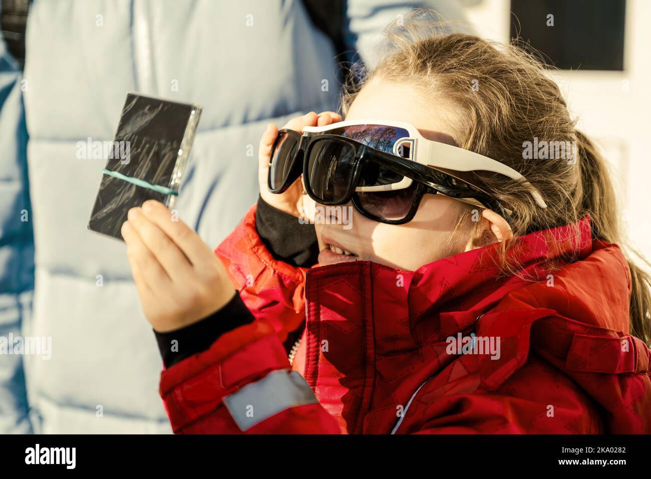 Kid watching solar eclipse with glass dark filter and several sunglasses, funny little girl looking eclipse of sun. Child viewing eclipse in sky. Conc Stock Photo
