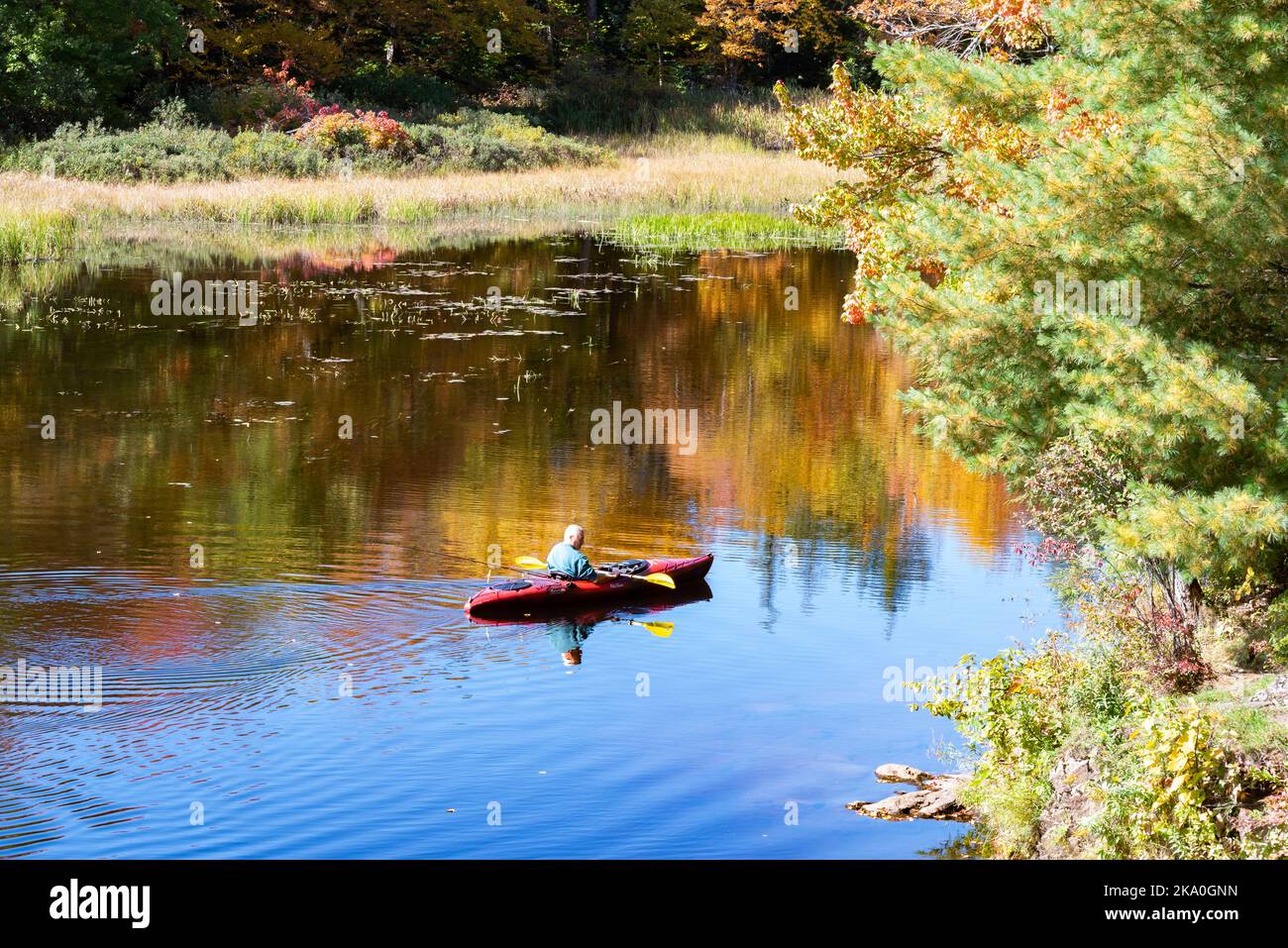 Senior man paddling a kayak and fishing on a lake in the Adirondack Mountains, NY USA Stock Photo