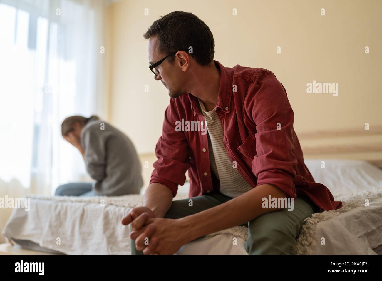 Confused man looks towards crying girl sits on opposite side of bed
