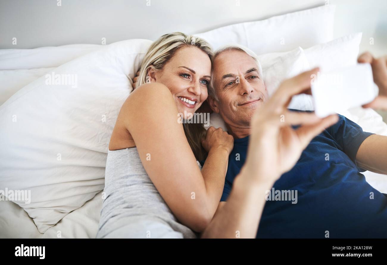 We take some amazing selfies together. an affectionate mature couple taking selfies in bed together at home. Stock Photo