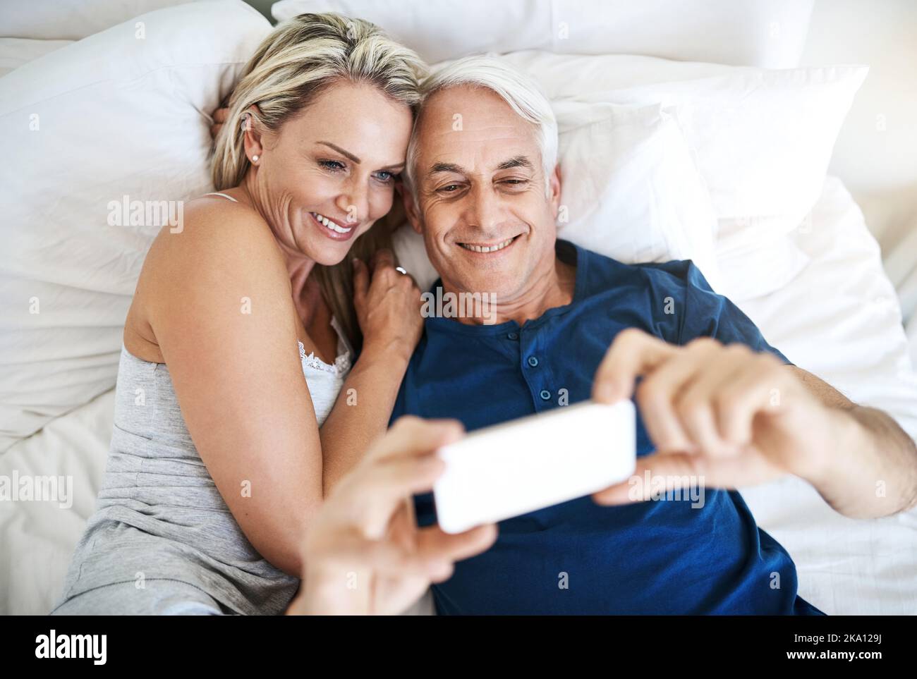 Lets say hello to the world with a selfie. an affectionate mature couple taking selfies in bed together at home. Stock Photo