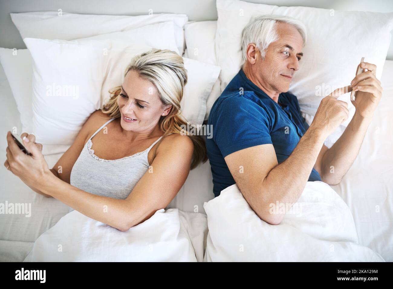 Caught up with their own connections. a mature couple using their cellphones in bed at home. Stock Photo