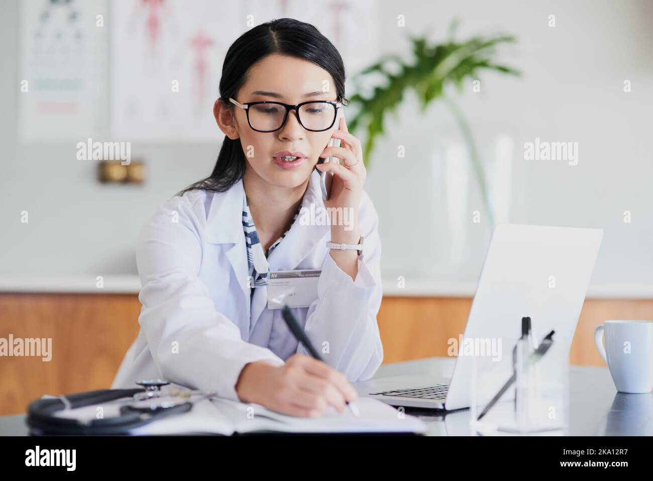 Alright, Ill book you in now. a young female doctor making notes while working in a hospital. Stock Photo