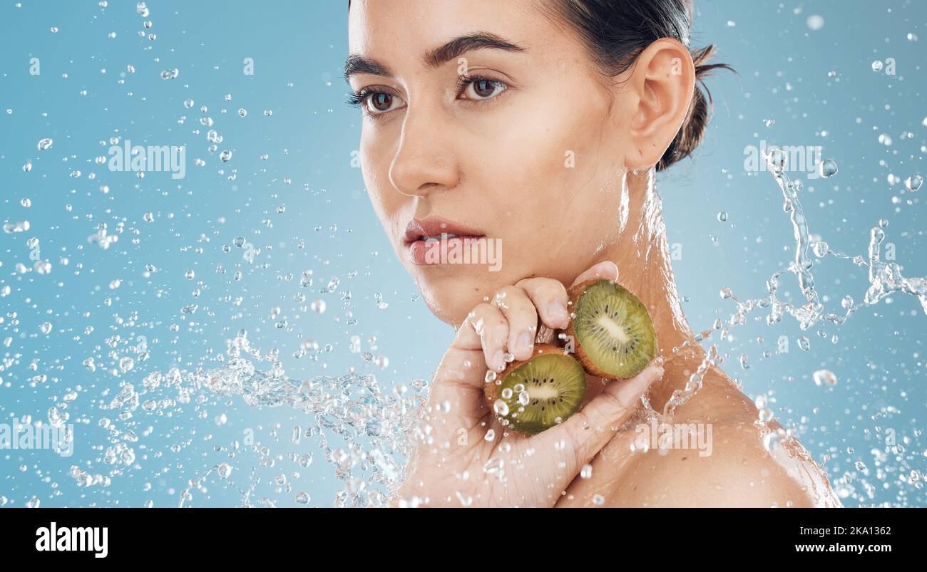 Beauty, water and kiwi with a model woman posing in studio on a blue ...