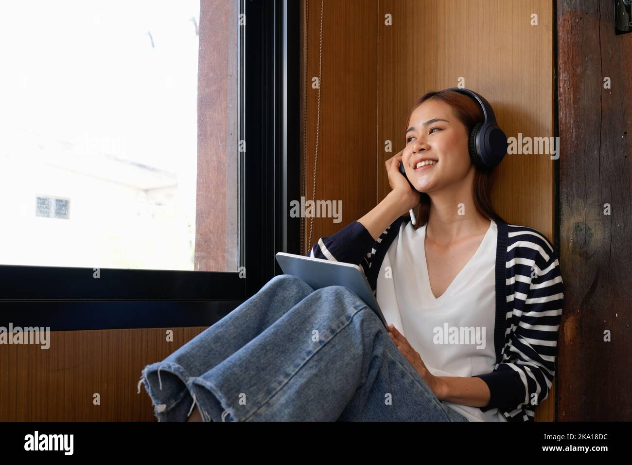 Young attractive asian female with headphone listening music on digital tablet. Stock Photo