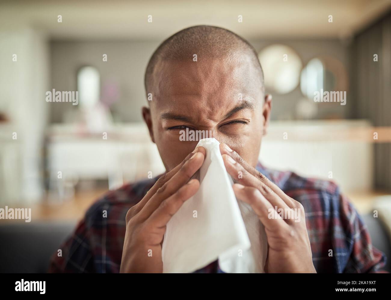 Why am I sick again. Portrait of an looking young man sneezing into a tissue while