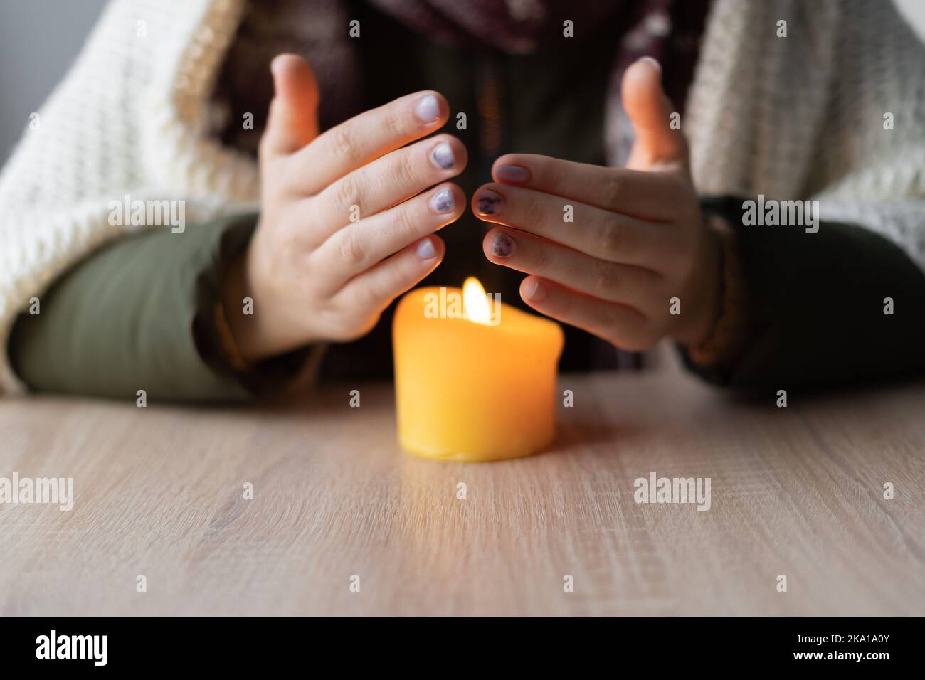Close up of womans hands warming from candle burning in warm clothes