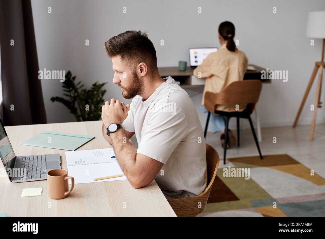 Side view of serious student or freelancer sitting in front of laptop by workplace and looking at screen during online lesson Stock Photo