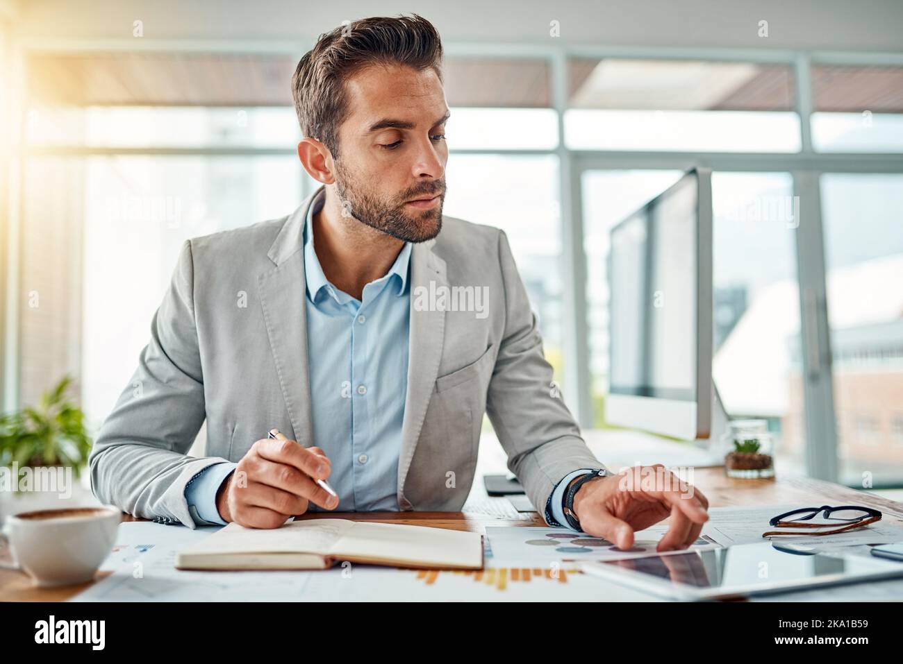 Making success happen. a handsome young businessman writing notes while using a digital tablet in an office. Stock Photo