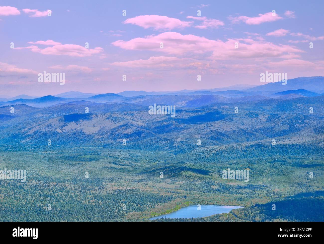 Mountain valley with blue lake among deep forests in pink morning light - idyllic summer landscape. Mountain peaks under blue morning mist and pink cl Stock Photo