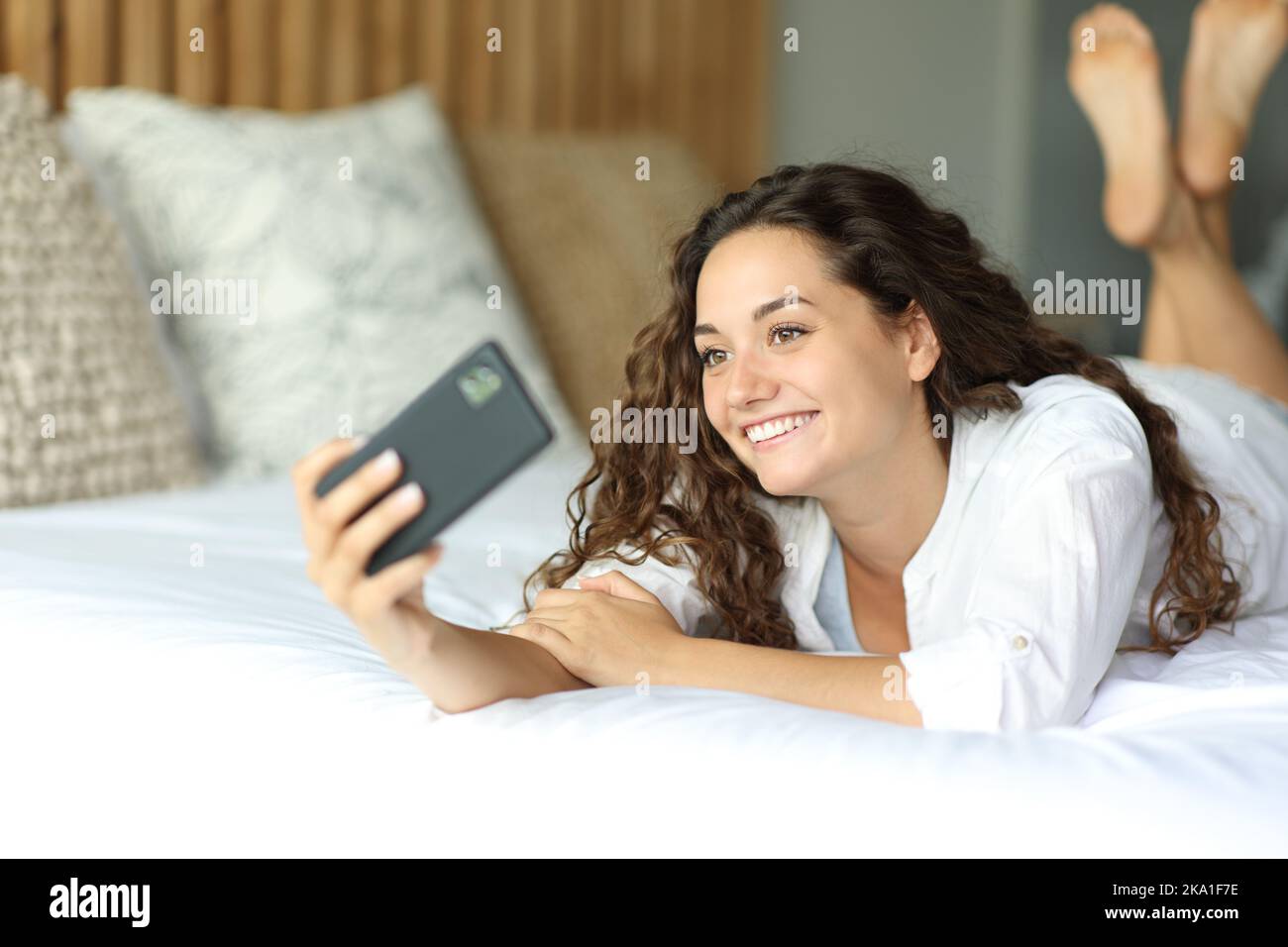 Happy woman lying on a bed taking selfie or recording video with phone