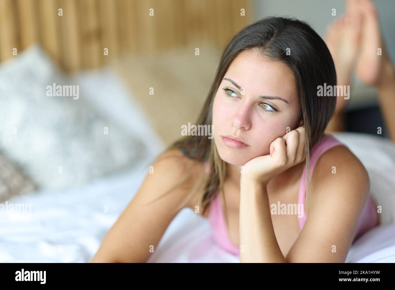 Distracted teen lying on a bed looking away at home Stock Photo