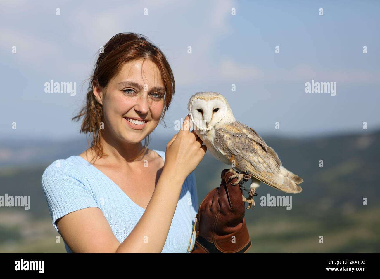 Falconer looking at camera caressing an owl in nature Stock Photo