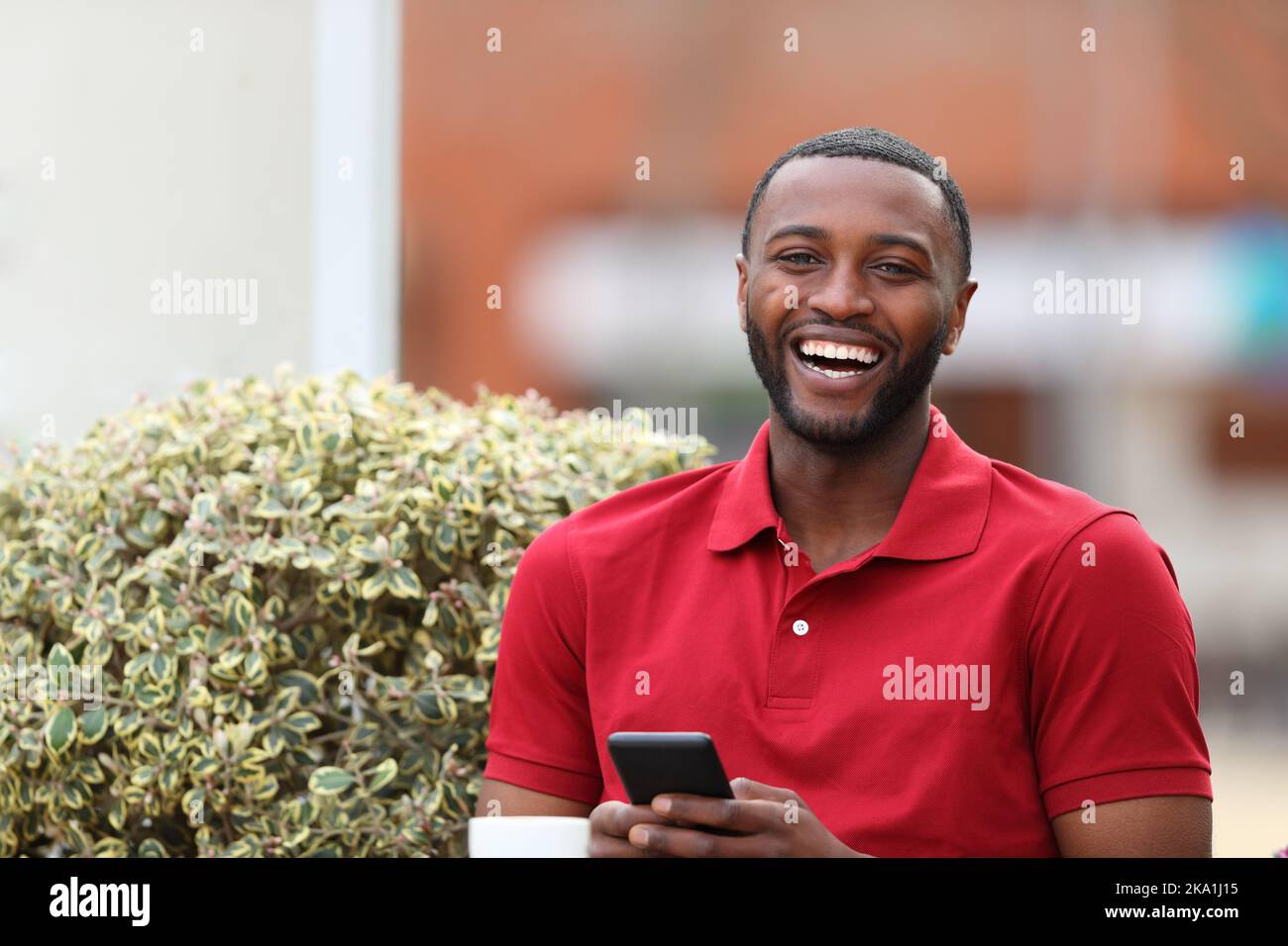 Happy black man holding mobile phone looking at you in a coffee shop Stock Photo