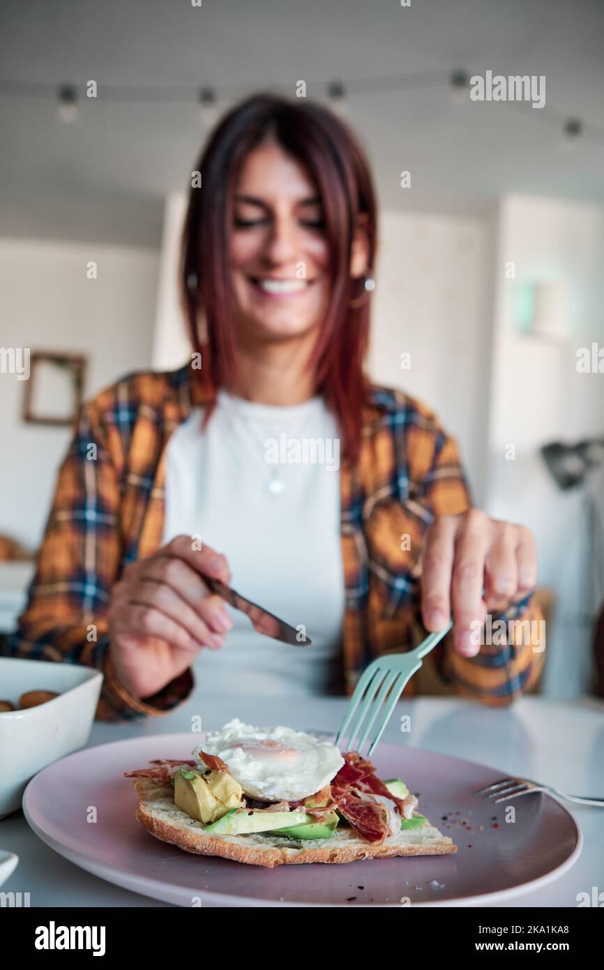 Woman smiling while eating an avocado toast in a cafe or restaurant. Stock Photo