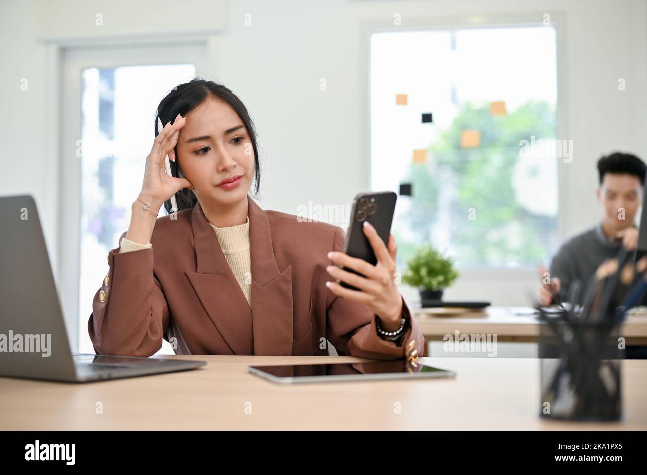 Phone, thinking and man by office window for career inspiration, job search  or online networking. Contemplating asian person or young entrepreneur  cellphone, smartphone or mobile app in workplace Stock Photo