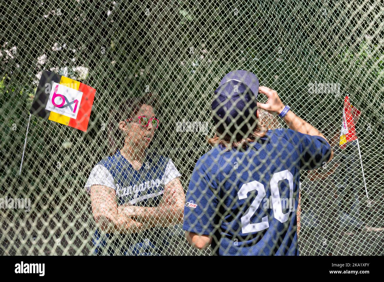 Two people in discussion behind a protective net, one seen from behind while drinking. Brussels. Stock Photo