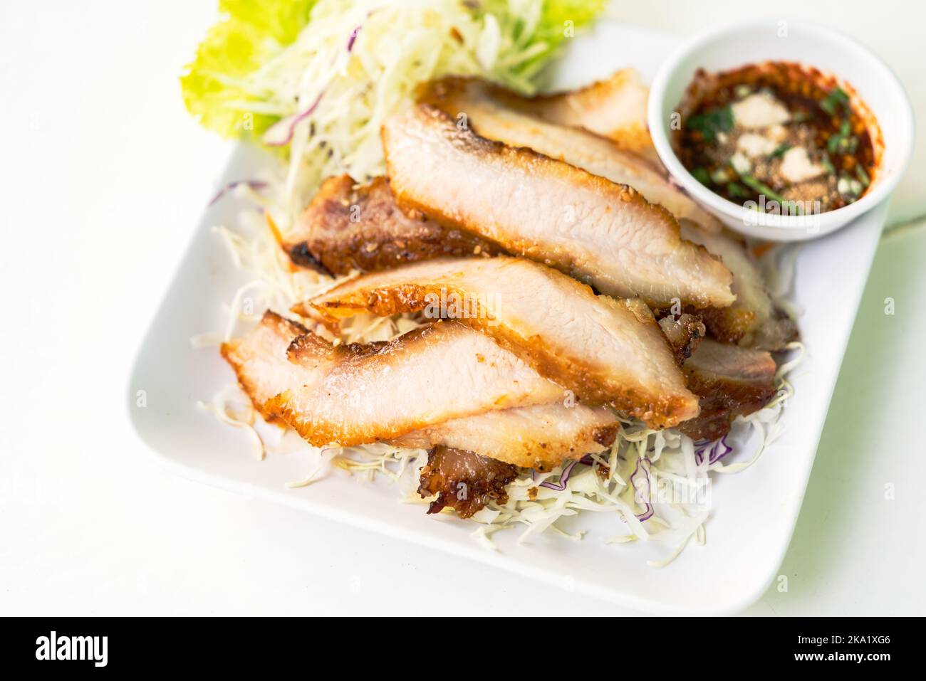 Grilled Pork Neck, close-up popular Thai food snack Grilled Pork Neck in white plate, bedding food with fresh vegetables, and spicy sauce, selected fo Stock Photo