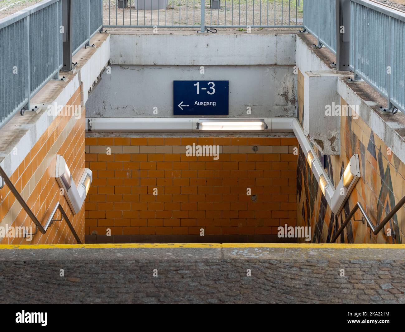 Tunnel entrance at a rail station. Path when changing the platform. Going downstairs into a dirty pedestrian underpass. Old yellow tiled exterior wall Stock Photo