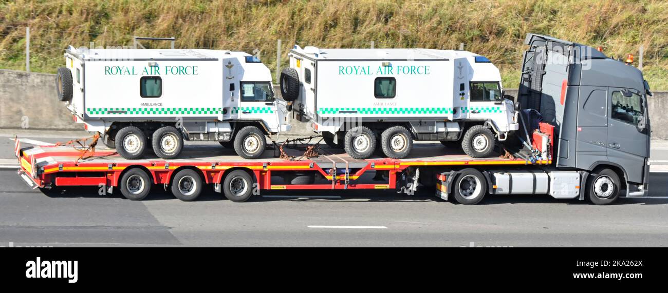 Grey Volvo hgv lorry truck driver articulated low loader trailer side view loaded transporting two Royal Airforce military ambulances UK motorway road Stock Photo