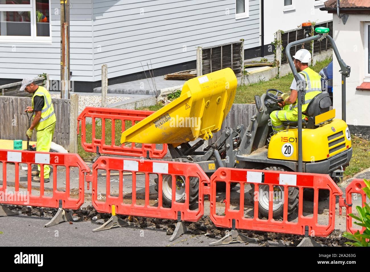 Labourer man working with dumper truck driver infrastructure project installing underground broadband fibre optic cable in pavement trench England UK Stock Photo