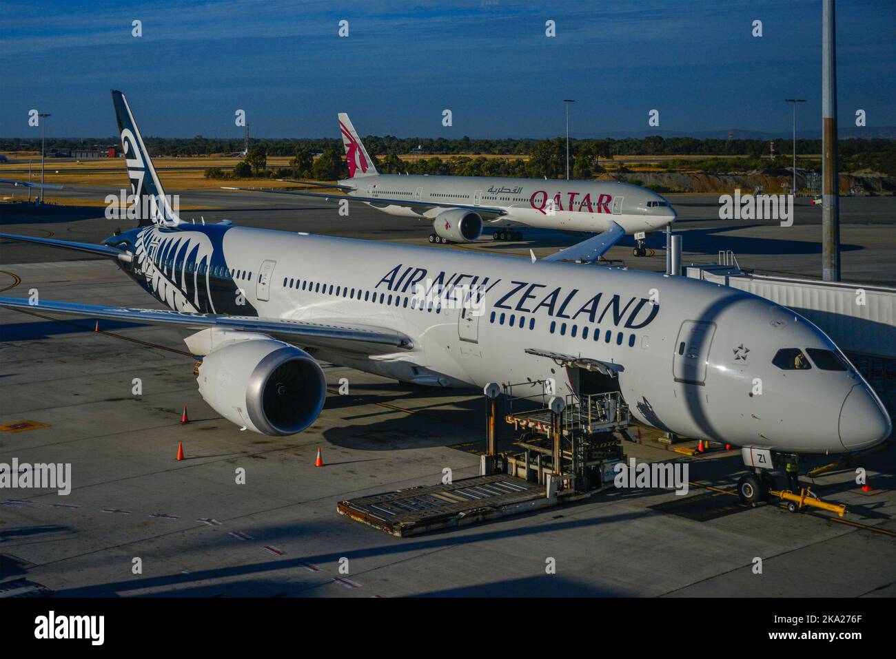 A stationary Air New Zealand Boeing 787 Dreamliner, and a Qatar Boeing 777 at an airport terminal. Stock Photo