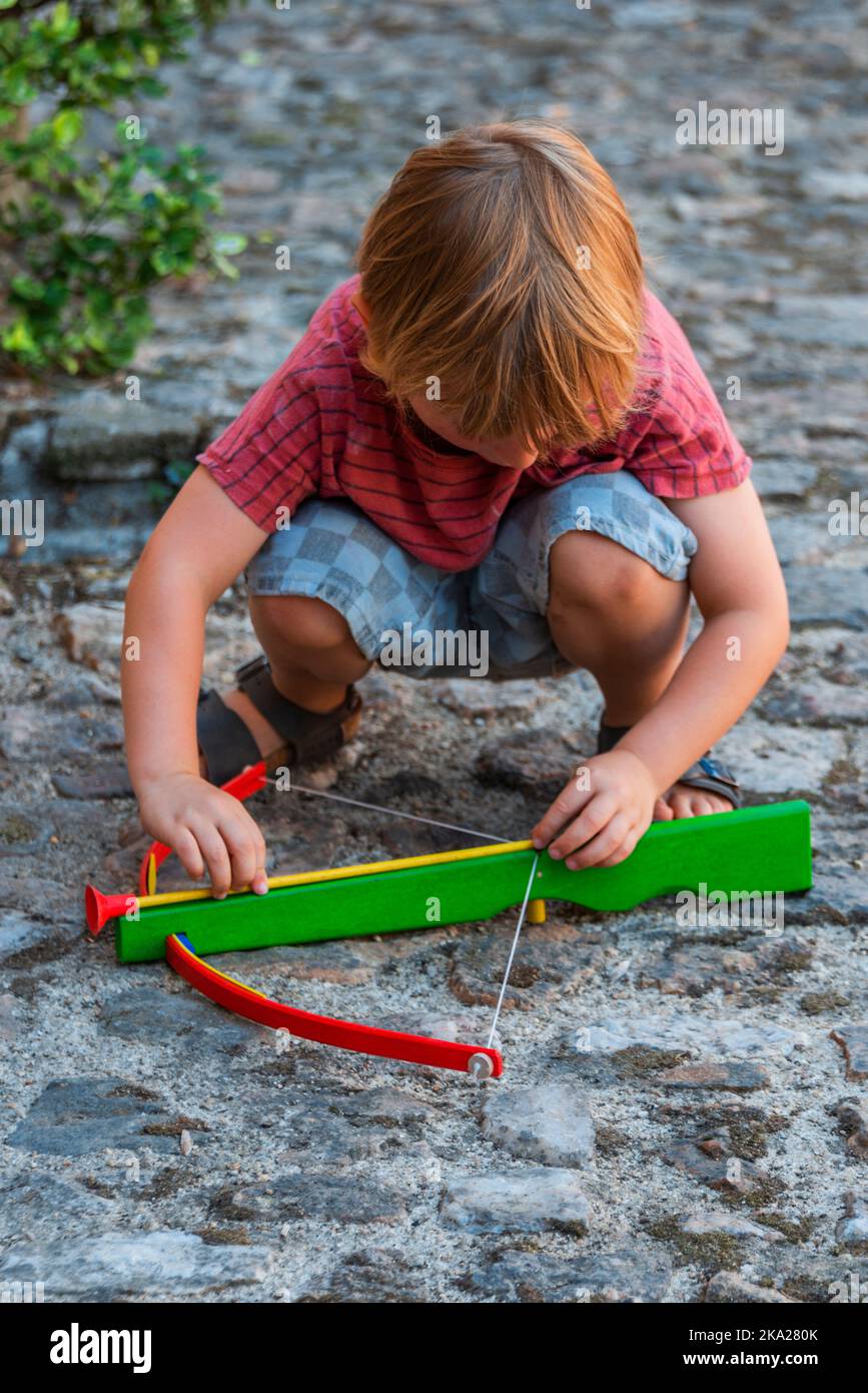 A portrait view of a young boy, crouching down and placing an arrow (bolt) on his crossbow. Stock Photo