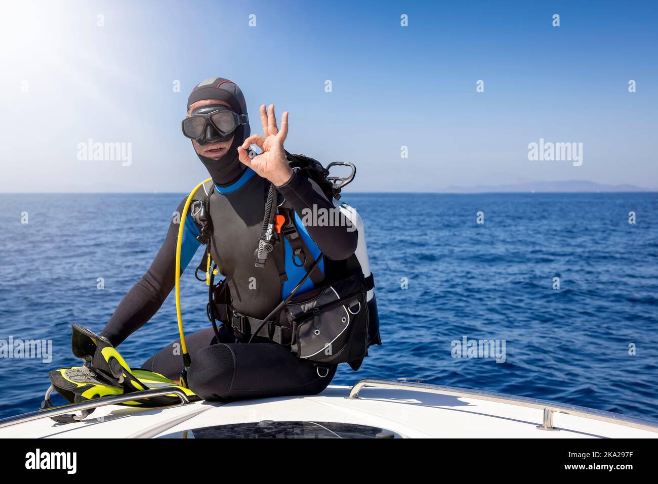 A scuba diver sits on a boat and signals the OK sign Stock Photo