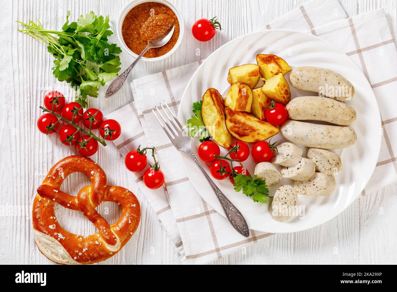 Weisswurst, bavarian white sausage of minced veal, pork back bacon, spices and parsley on white plate with roast potatoes, fresh tomatoes, pretzels, h Stock Photo