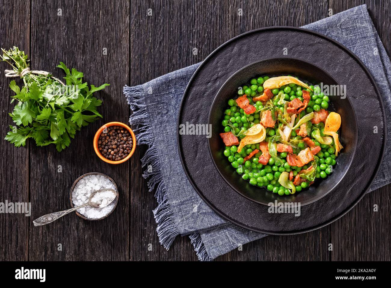 petits pois, french dish of tender, new-season peas braised in chicken stock with lettuce, onion bulbs and speck, cut into lardons, served in black bo Stock Photo