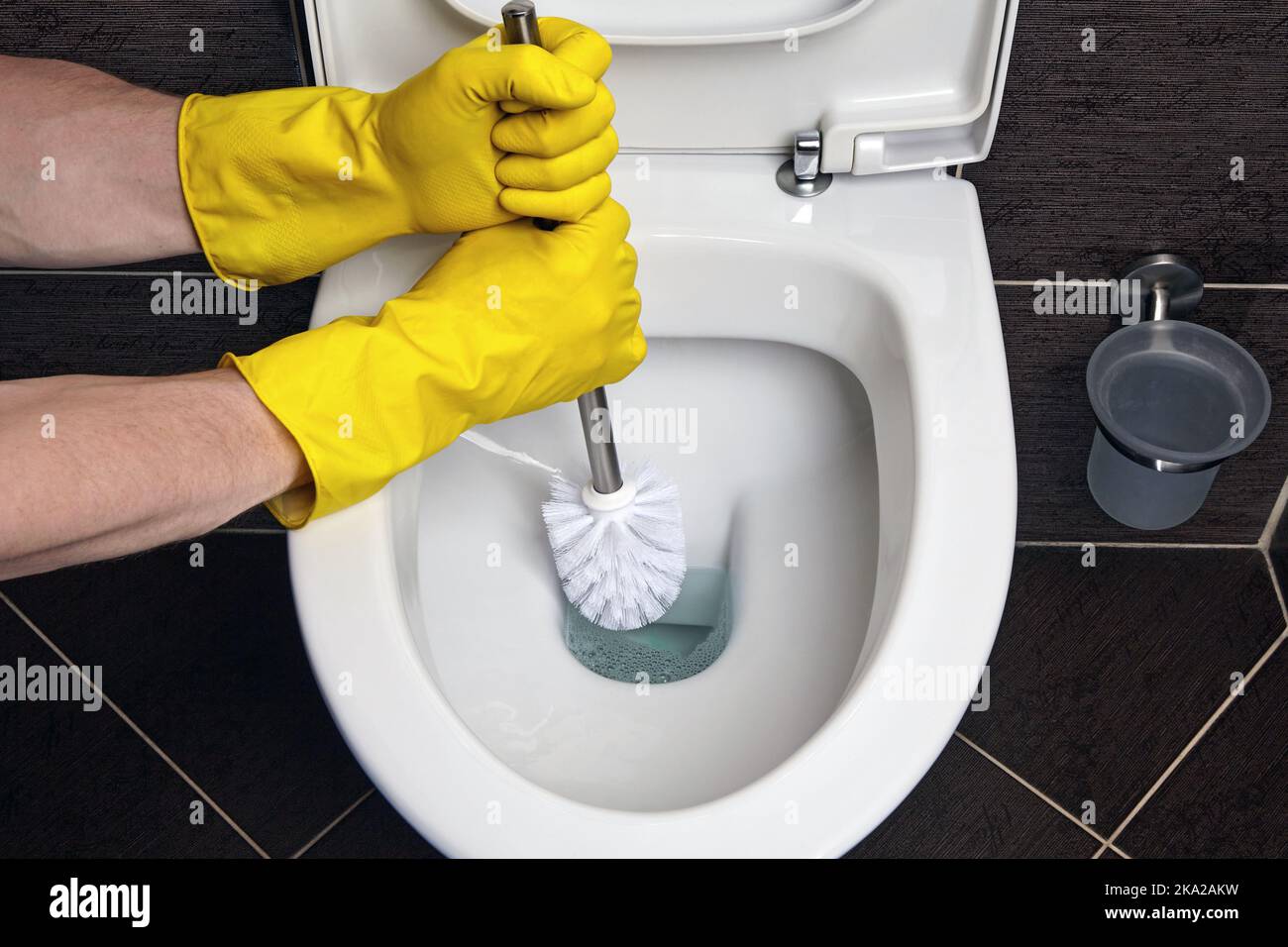 Hands in yellow rubber gloves clean the toilet bowl with a brush Stock