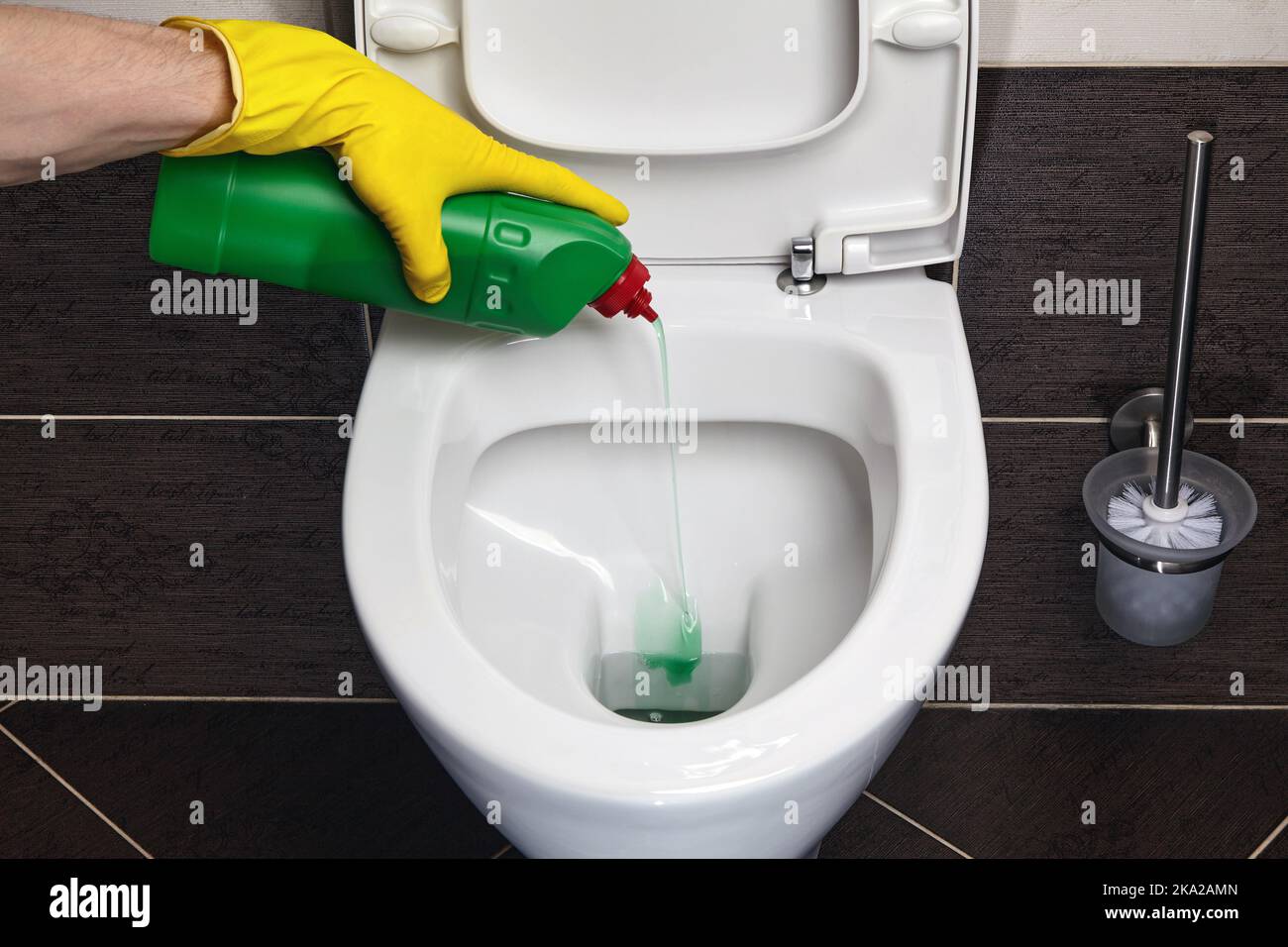 Hands in yellow rubber gloves pour disinfectant into the toilet Stock