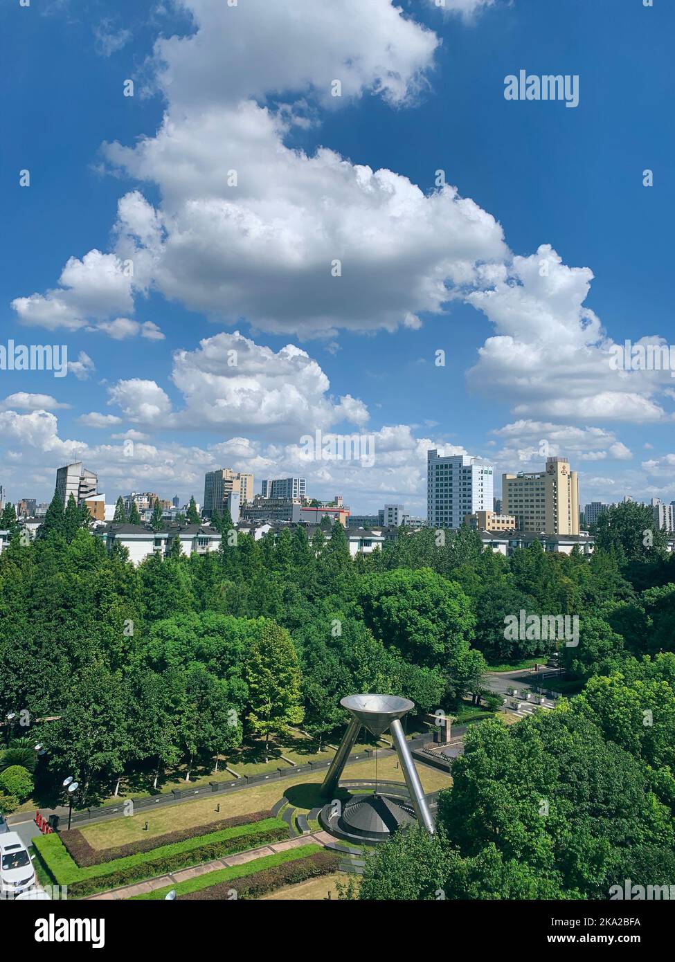 A Vertical shot of buildings behind green trees under cloudy sky Stock ...