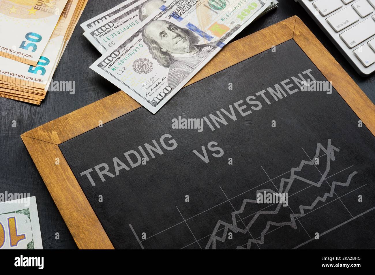 Money and blackboard with words trading vs investing. Stock Photo