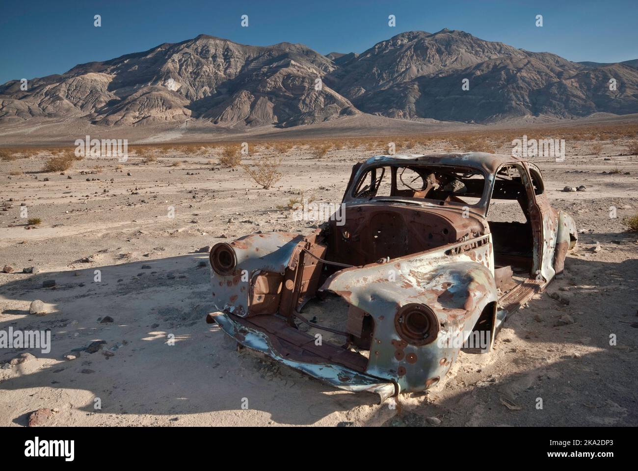Old car wreck, riddled with bullets, Four Mine Road in Panamint Valley, Inyo Mountains in distance, Mojave Desert, Death Valley Natl Park, California Stock Photo