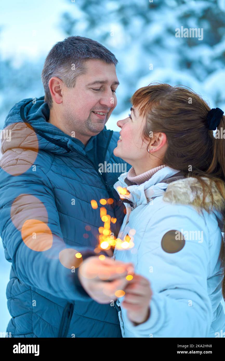 A young couple in love embracing in the winter woods holding sparklers ...