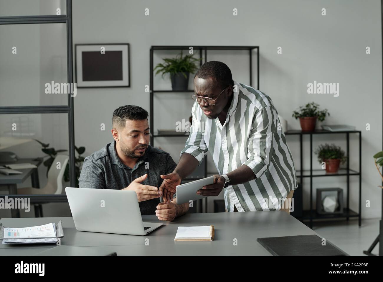Two young multicultural colleagues with mobile gadgets arguing about online data while preparing presentation together in office Stock Photo