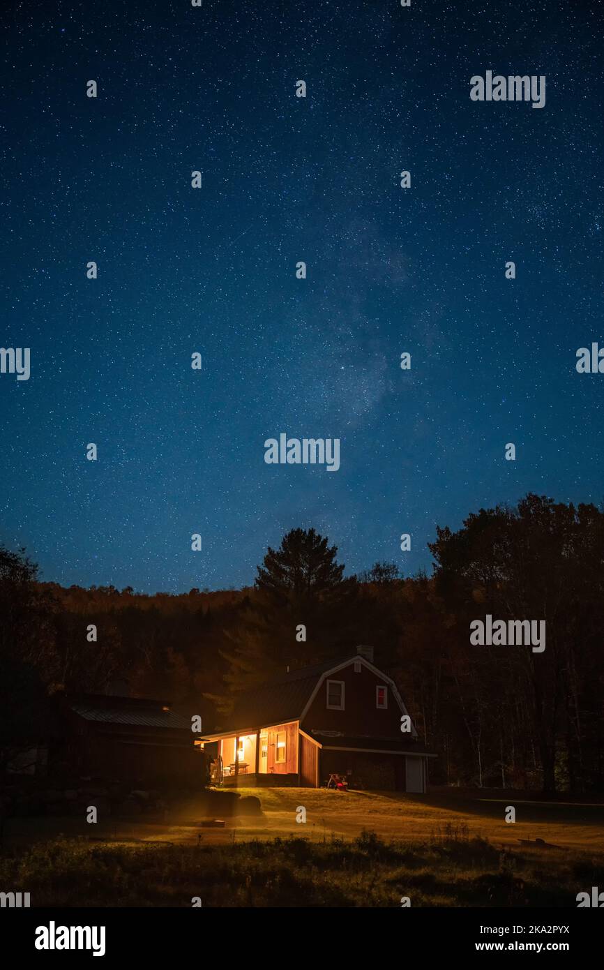A vertical shot of a small house with light on under the starry night ...