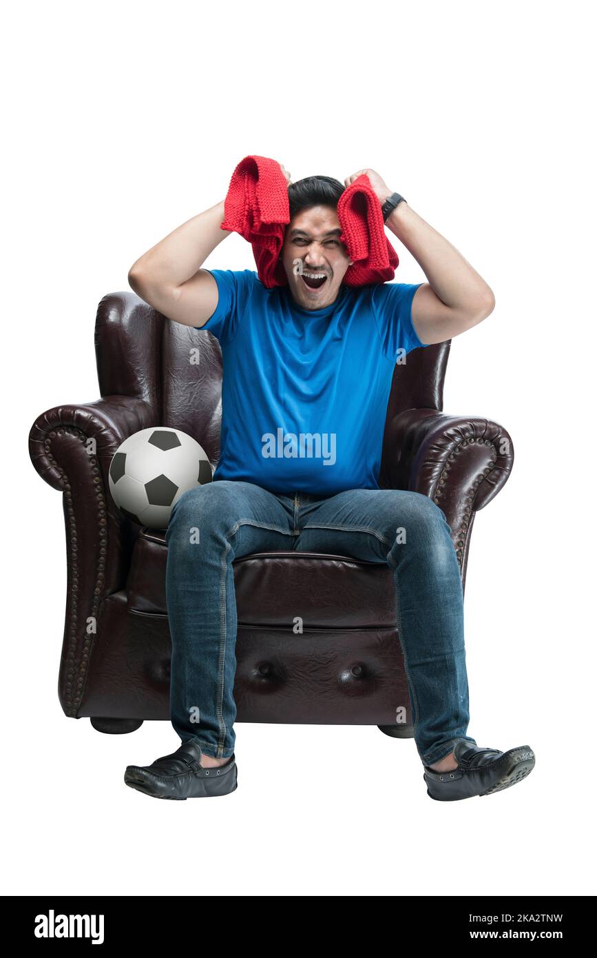 Asian man with a scarf and the ball sitting on the couch with a disappointed expression isolated over white background Stock Photo