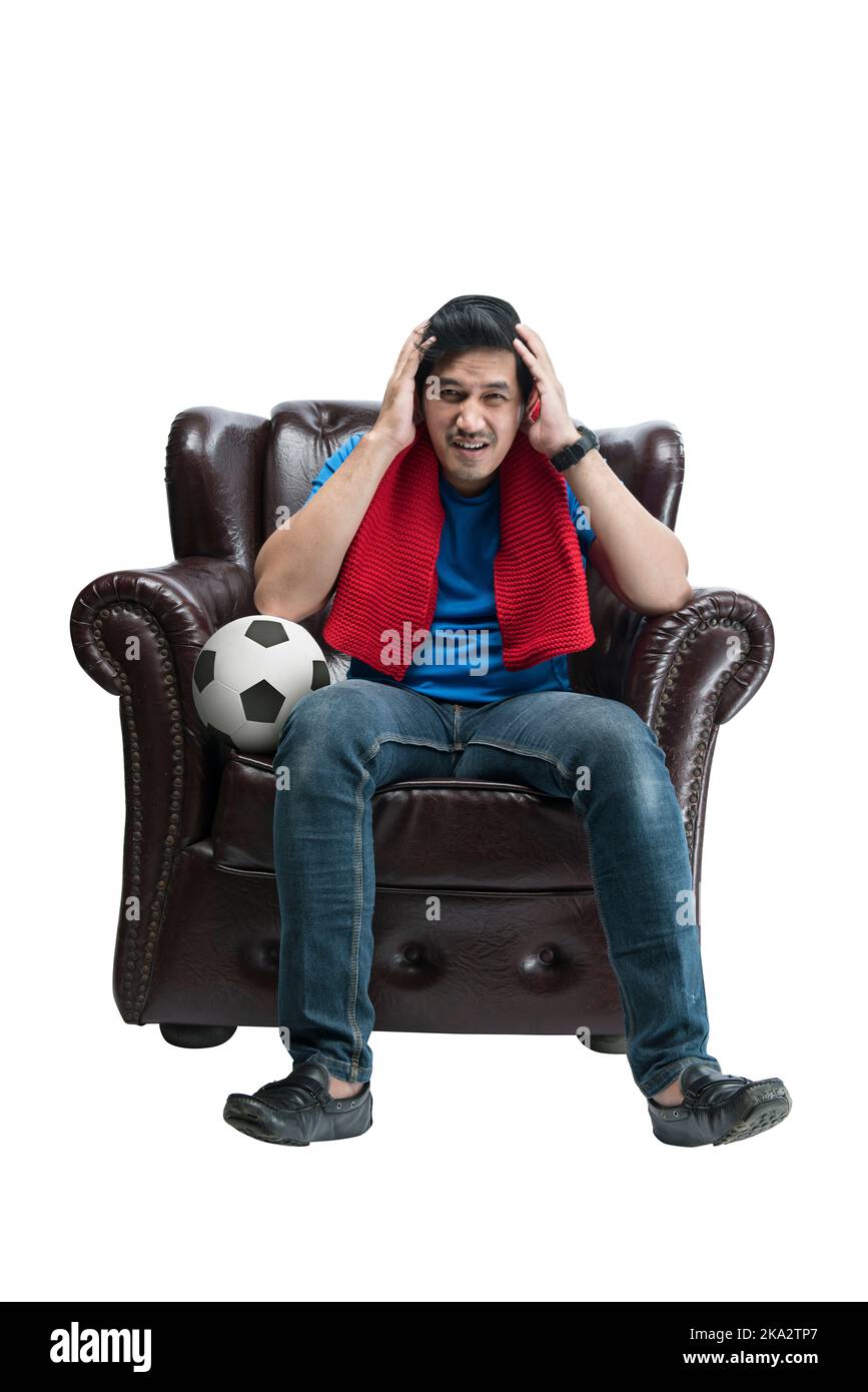 Asian man with a scarf and the ball sitting on the couch with a disappointed expression isolated over white background Stock Photo