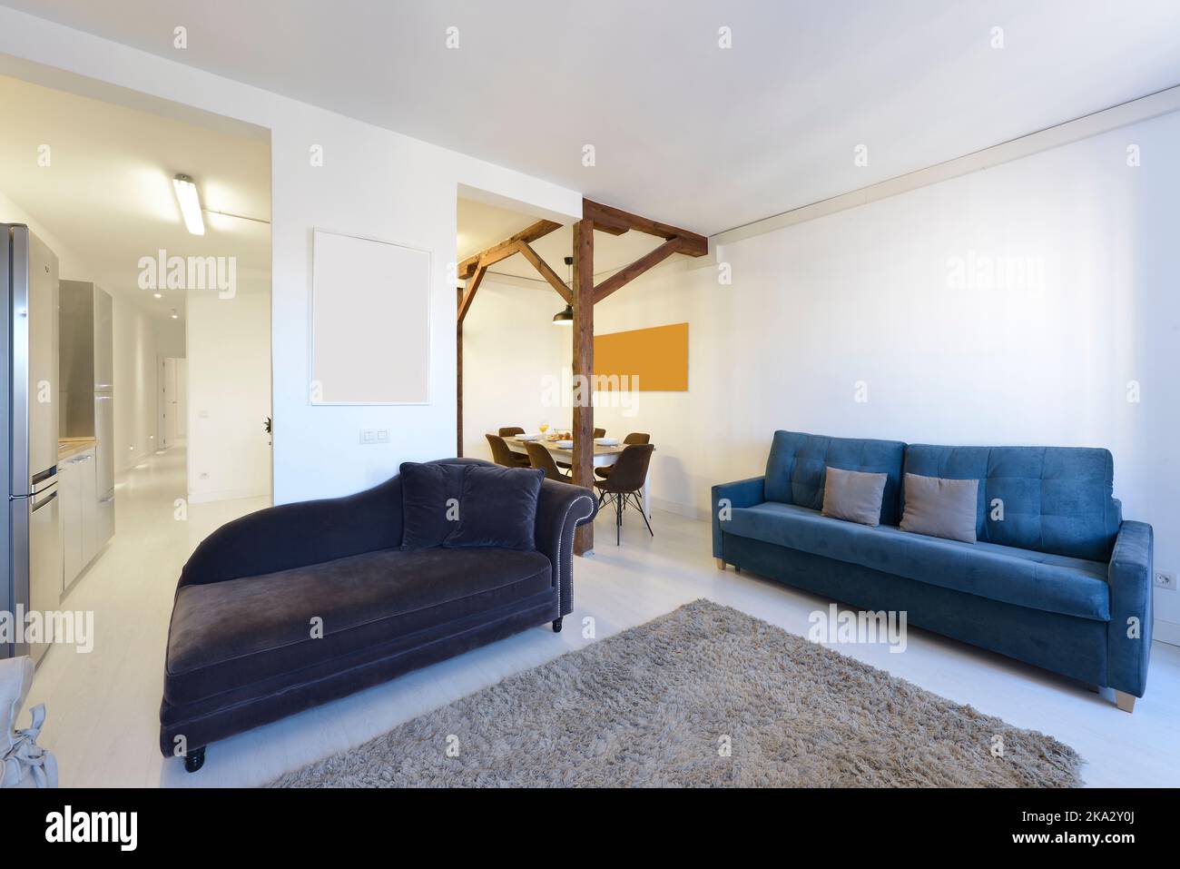 Living room with wooden beams and blue sofas and open plan kitchen with