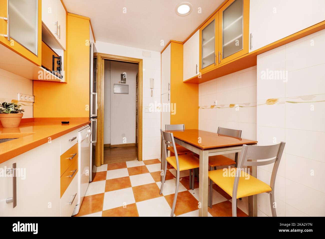 Kitchen design with bright orange and white cabinets with matching dining table and gray metal chairs Stock Photo