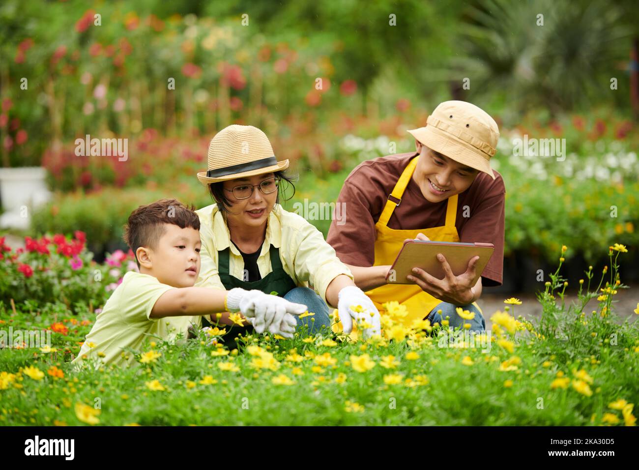 Smiling father taking notes in document on tablet computer when mother and son checking flowers Stock Photo